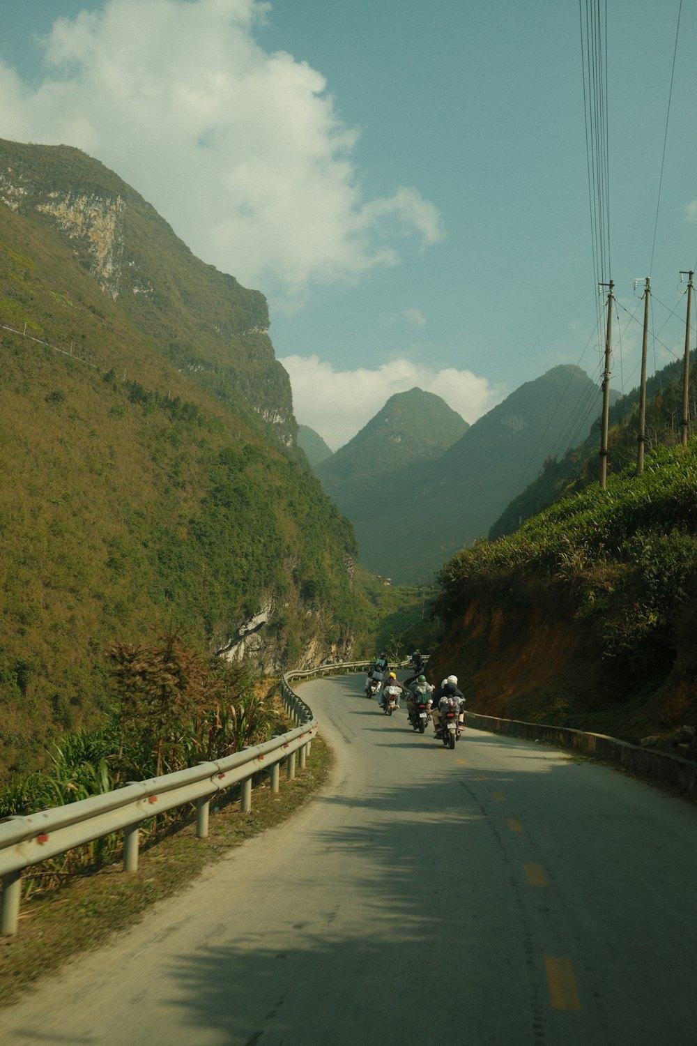Riders on a winding valley road between green mountains